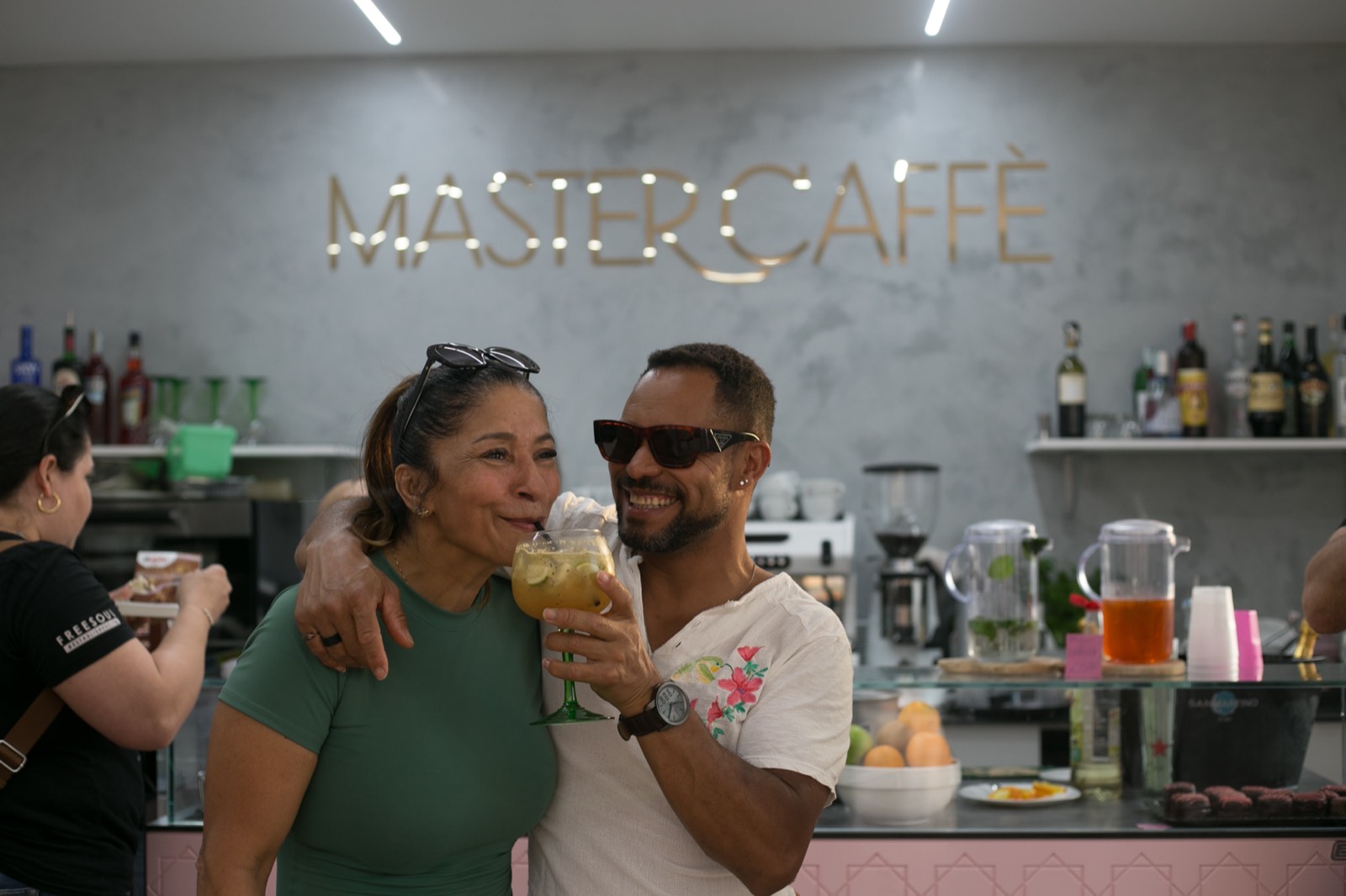 Due ospiti brindano davanti alla scritta dorata Master Caffe