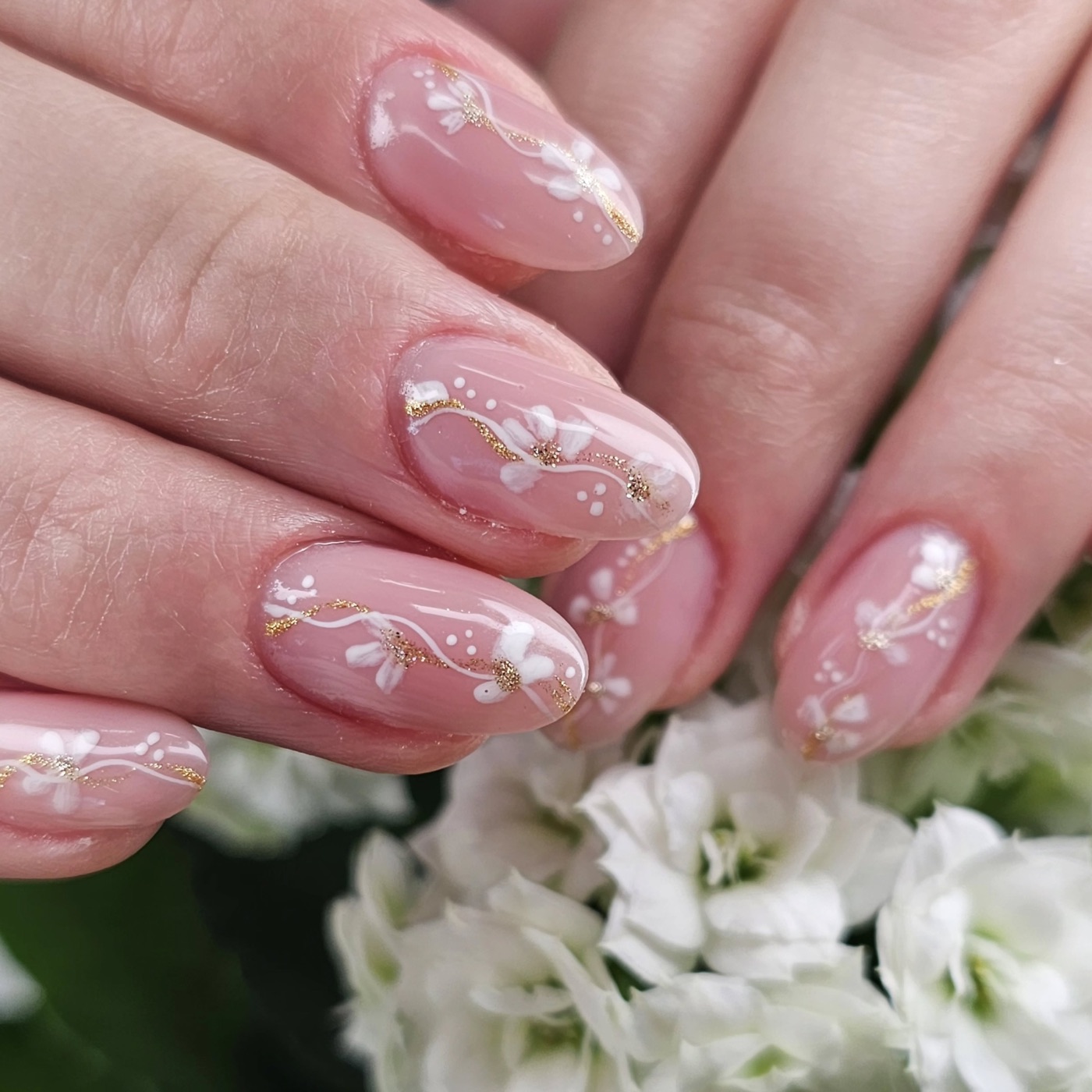 Nail art rosa con decori floreali bianchi e dettagli dorati